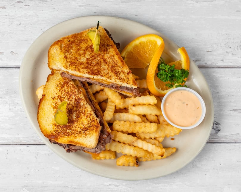 Grilled sandwich with meat and cheese, crinkle-cut fries, orange slices, and dipping sauce on a plate.