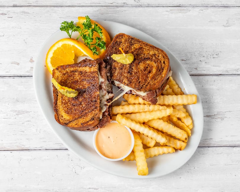 A grilled sandwich with melted cheese and meat, crinkle-cut fries, sauce, and orange slices.