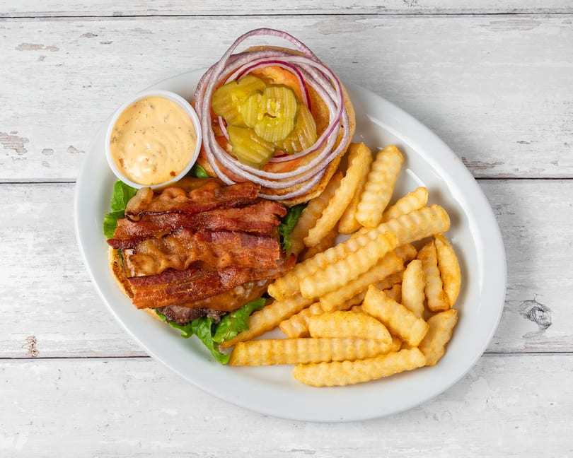Bacon cheeseburger with lettuce, tomato, onion, pickles, and a side of crinkle-cut fries and dipping sauce.