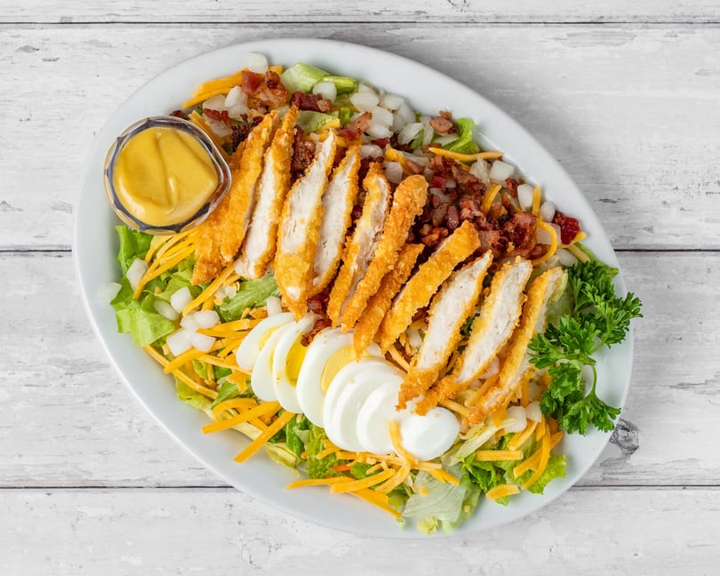 Crispy chicken salad with lettuce, cheese, bacon, hard-boiled eggs, and a side of honey mustard.